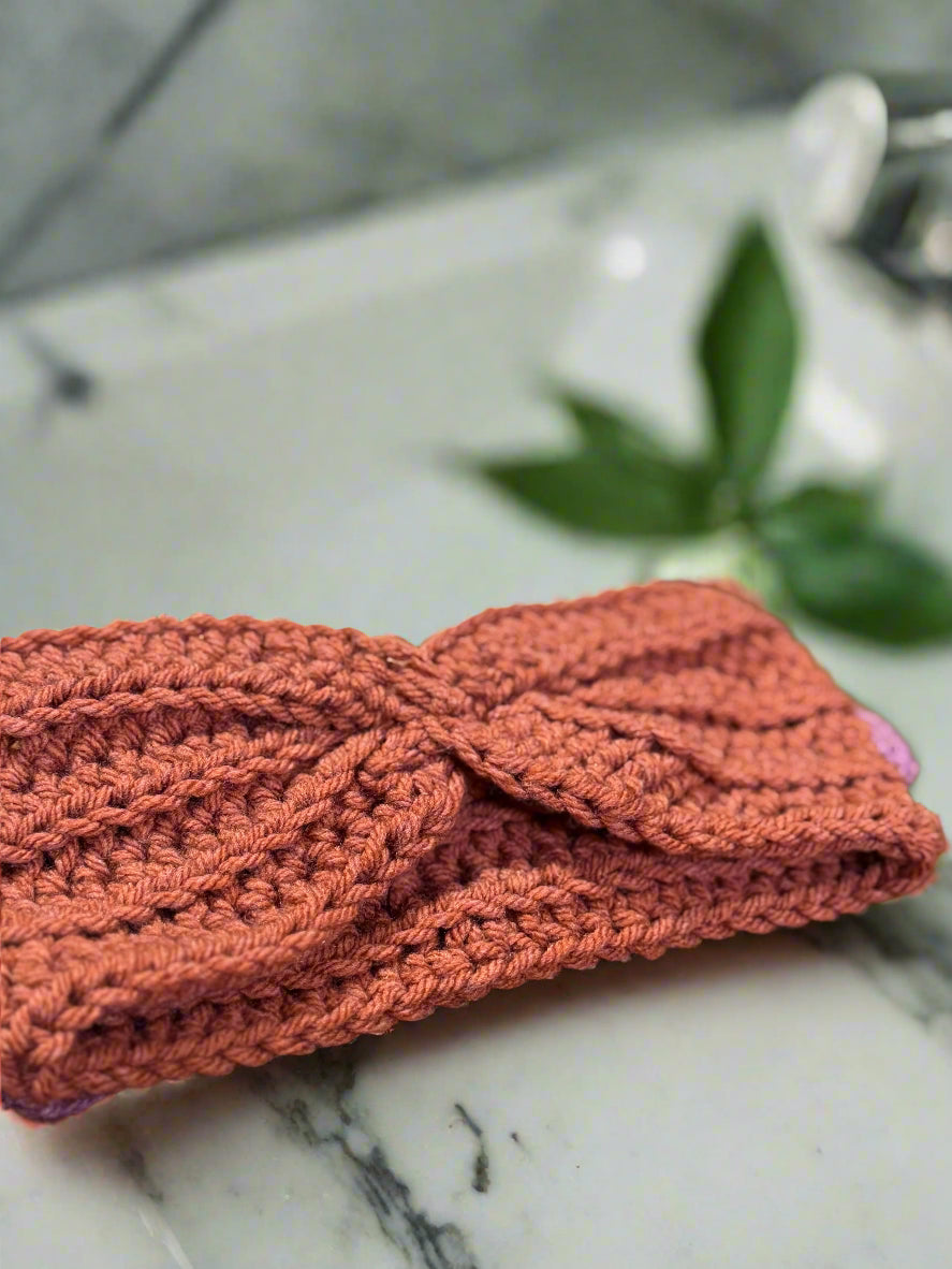 Knitted headband on a wooden surface with yarn and a mug in the background